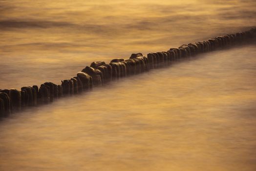 A photograph of wooden breakwater and seagulls at sunset on the Baltic Sea