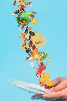 Male hands holding an empty white bowl on blue background. Candied fruits and nuts flying above the bowl. Stock photo of nutrient and healty food. Conceptual photo of vegan and vegetarial food and meal.