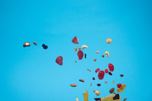 Dried and candied fruits and nuts flying on blue background. Stock photo of healty and nutrient food. Conceptual photo of vegan and vegetarian healty food.