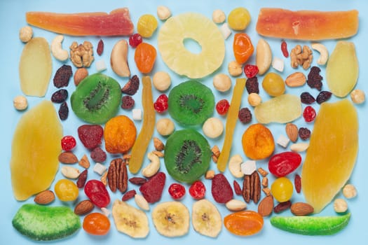 Flat lay photo of dried and candied fruits and nuts on blue background. Includes pamelo, papaja, ginger, walnut, pecan nut, cumquat, peanut, kiwi, apricot, mango, cherry and strawberry.