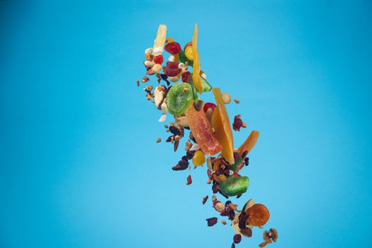 Dried and candied fruits and nuts flying on blue background. Stock photo of healty and nutrient food. Conceptual photo of vegan and vegetarian healty food.