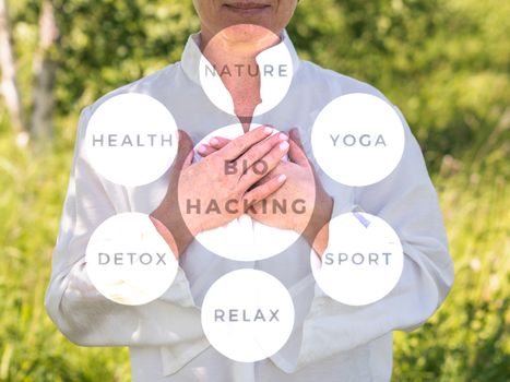 Women's hands on heart in meditating. Mature woman. Biohacking, yoga, relax, meditacion on nature concept