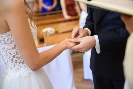 the bride and groom during the wedding ceremony put wedding rings on their fingers.