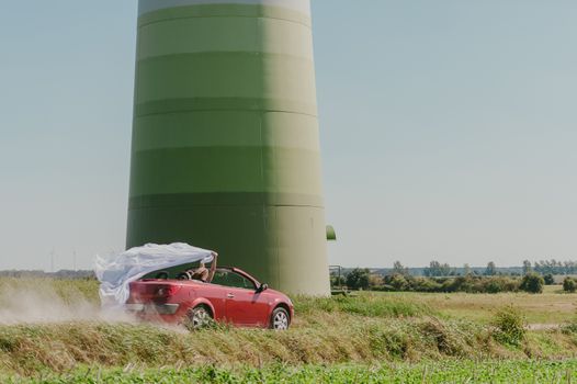 Bride and groom at a photo session in the nature. Moving fast red car with veil outside