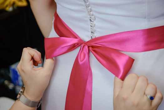 Bridesmaid helping slender bride lacing her wedding white dress, buttoning on delicate lace pattern with fluffy skirt on waist. Morning bridal preparation details newlyweds. Wedding day moments, wear.