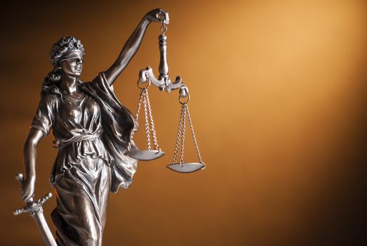 Bronze statue of Justice carrying a sword and holding up scales representing law and order over a brown background with copy space
