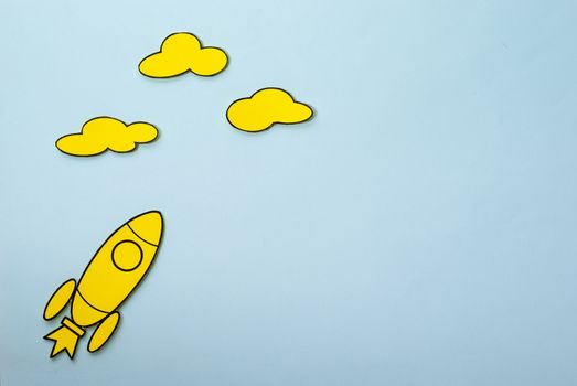 Little yellow rocket flying high aiming for the clouds in a concept of ambition and success over a blue background with copy space