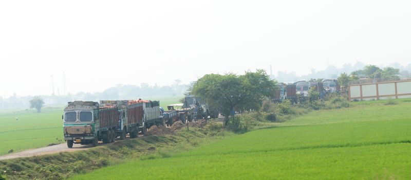 Long queue traffic of heavy cargo lorry trucks Vehicles waiting in line on a village highway unpaved road. India is largest land service interstate network in world. West Bengal, India Asia May 2019