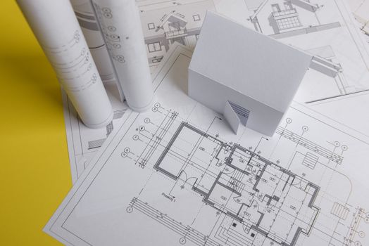 White family paper house, house projects plan and blueprints in the background. Minimalistic and simple concept, style. Horizontal orientation. View from above.