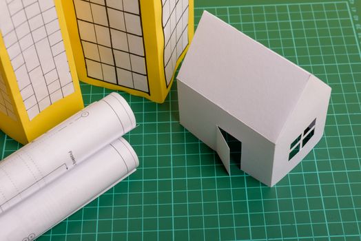 White family paper house, house projects plan and blueprints in the background. Minimalistic and simple concept, style. Horizontal orientation. View from above.