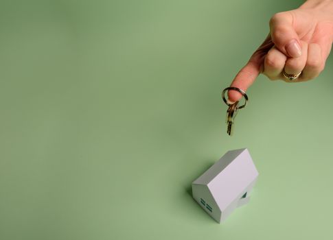 White family paper house. House keys in hand on mint background paper. Minimalistic and simple concept, style. Copy space. Vertical orientation. Family moving or removal concept.