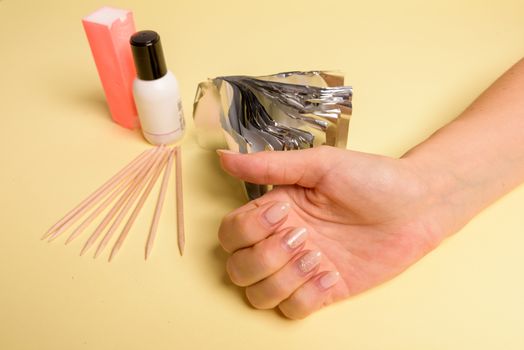 The procedure for removing varnish from nails hybrid nails in progress. Gel nail polish remover foils on woman's hands
