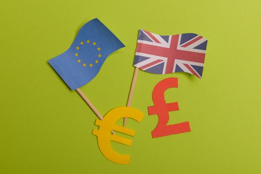 Paper yellow symbols of euro and pound currency on green background. View from above with copy space. EU and United Kingdom flags