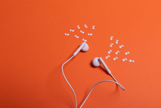 white earphones and white paper notes on orange background. view from above