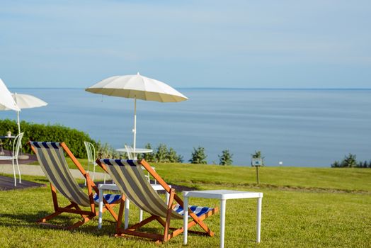 Empty beach chair on meadow on summer time. Sunlight and sea in the background. Coast line