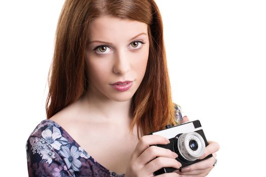 Close up portrait of a beautiful young girl holding a retro film camera in hands while standing and looking at the camera, isolated on white background. Attractive female holding old fashioned camera.