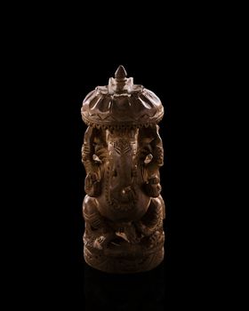 A low light photo of indian god Ganesh statuette. Figurine made of sandalwood. Background is black, statuette is isolated on black bakground. Indian culture figurine photo.