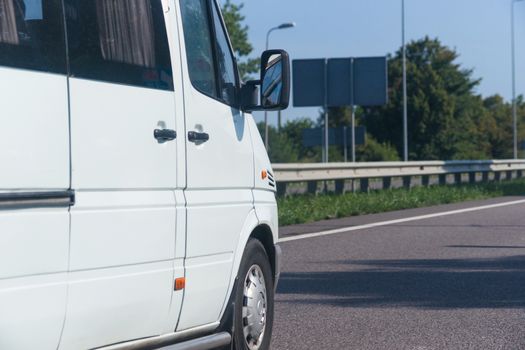 Side view of white passenger bus on the sunny road.