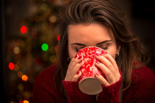 Evening, leisure, christmas, winter and people concept - happy young woman with cup of coffee or tea at home