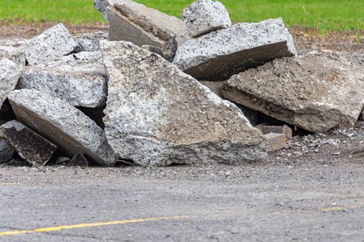 Fragments of broken asphalt and concrete are piled on the ground in a parking lot. The stone shards were dug up and torn out of the ground by an excavator during construction to renovate the pavement.