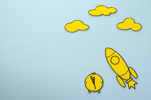 Little yellow rocket speeding through space with a clock and clouds over a blue sky background with copy space