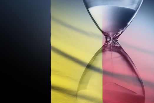 Flag of Belgium with superimposed hourglass with running sand conceptual of deadlines, countdown, passing time, urgency, crisis and time management