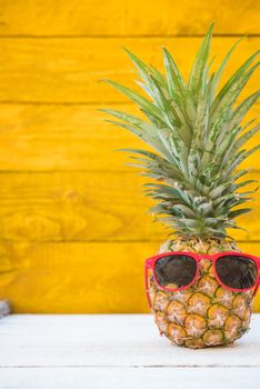 Holiday pineapple have sunglasses on yellow wooden background, tropical holiday concept