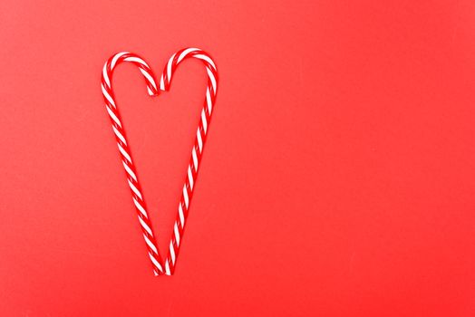 Two candy canes made making Heart of Christmas candies on red background with copy space