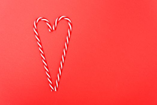 Two candy canes made making Heart of Christmas candies on red background with copy space