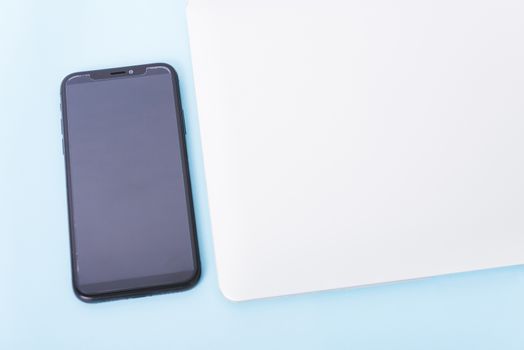 Top view close cover laptop computer notebook, smart phone and wireless mouse isolated on blue background