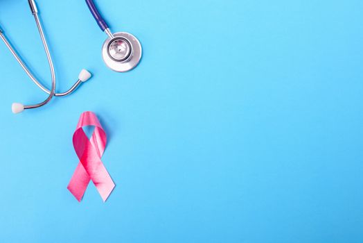 Breast cancer month concept, flat lay top view, pink ribbon and stethoscope on blue background with copy space for your text