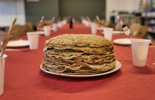 set table with a plate with a stack of pancakes on a red tablecloth with cups for drinks