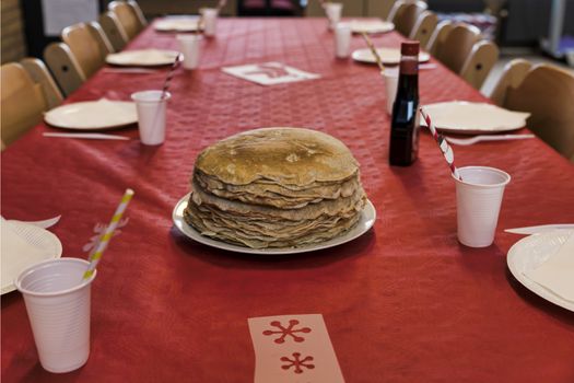 set table with a plate with a stack of pancakes on a red tablecloth with cups for drinks