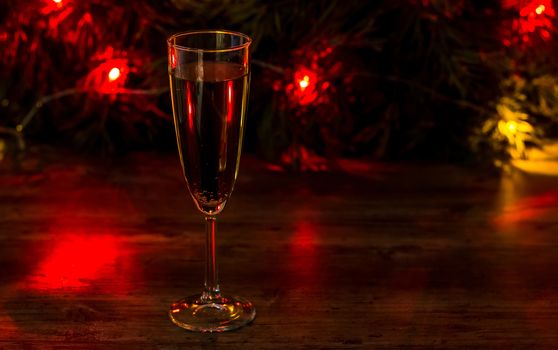 A glass of champagne on the background of a Christmas tree with a garland and bokeh. New year 2020 and Christmas