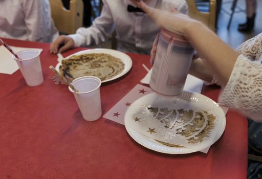 children at the table busy sprinkling pancakes with powdered sugar for the Christmas meal