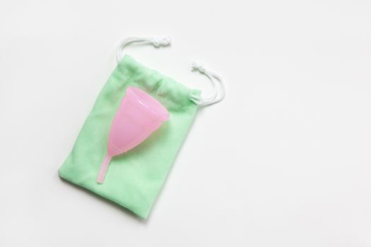 Pink menstrual cup on green small bag on white background. Concept zero waste, savings, minimalism, these days. Feminine hygiene product, flat lay, copy space. Horizontal.