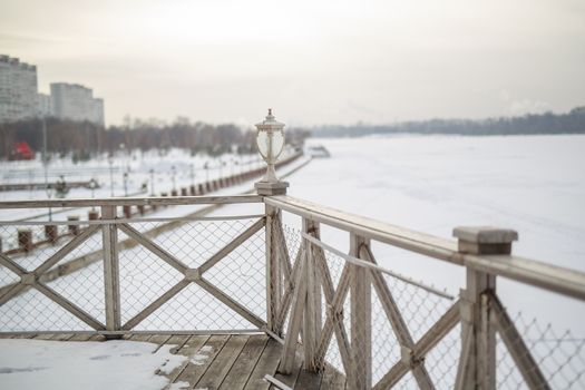 white snow on the wooden vintage open deck, old peeling paint light milk color, steel and copper lanterns hanging on the wall, snowy winter, snow lies on the river and the far shore of the earth is vi