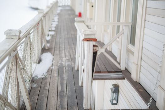 white snow on the wooden vintage open deck, old peeling paint light milk color, steel and copper lanterns hanging on the wall, snowy winter, snow lies on the river and the far shore of the earth is vi