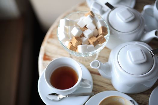 morning Cup of tea stands on the edge of the wooden Desk, square pieces of sugar in the sugar bowl, tea kettle, coffee kettle