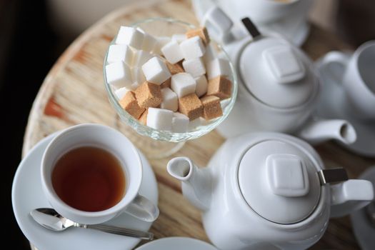 morning Cup of tea stands on the edge of the wooden Desk, square pieces of sugar in the sugar bowl, tea kettle, coffee kettle