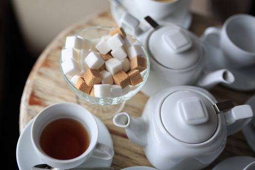 morning Cup of tea stands on the edge of the wooden Desk, square pieces of sugar in the sugar bowl, tea kettle, coffee kettle