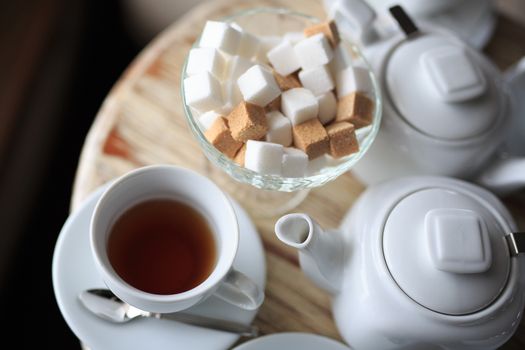 morning Cup of tea stands on the edge of the wooden Desk, square pieces of sugar in the sugar bowl, tea kettle, coffee kettle