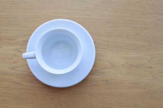 one pure white ceramic Cup and saucer without drink sits on a wooden table in the afternoon sunlight the view from the top