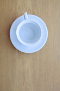 one pure white ceramic Cup and saucer without drink sits on a wooden table in the afternoon sunlight the view from the top