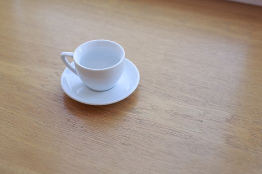 one pure white ceramic Cup and saucer without drink sits on a wooden table in the afternoon sunlight