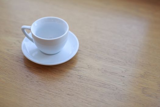 one pure white ceramic Cup and saucer without drink sits on a wooden table in the afternoon sunlight