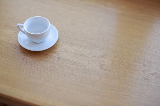 one pure white ceramic Cup and saucer without drink sits on a wooden table in the afternoon sunlight