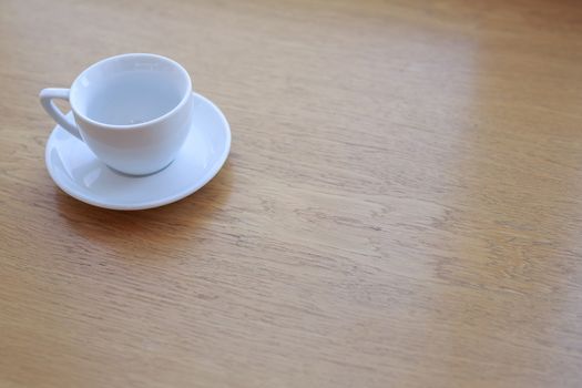 one pure white ceramic Cup and saucer without drink sits on a wooden table in the afternoon sunlight