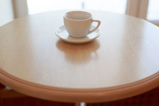 one pure white ceramic Cup and saucer without drink sits on a wooden table in the afternoon sunlight