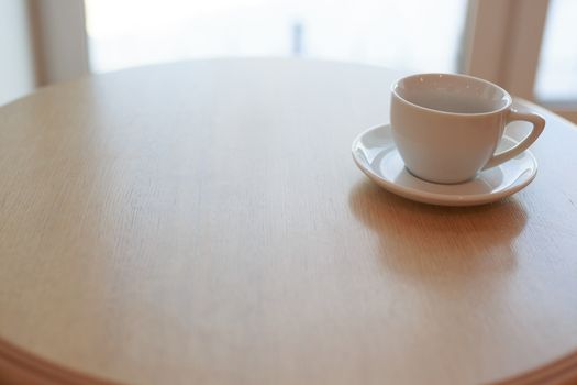 one pure white ceramic Cup and saucer without drink sits on a wooden table in the afternoon sunlight